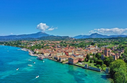 Italien, Gardasøen, Lazise.... hvor skal jeg snart starte? For mig, et af de mest perfekte feriesteder, jeg har besøgt. Måske fordi jeg har været der, siden jeg var lille.  Hvis du ikke har været ved Gardasøen, så tænker du måske lettere skeptisk over det, at skulle holde ferie ved en sø, for hvad er dog det for et vandhul at skulle bade i? Men sådan er det ikke. På de bedste dage - og dem er der mange af - er vandet så klart, at du kan se dine fødder på sandbunden. Andre dage har det blæst så tilpas meget, at sandbunden stadig er i oprør. Det faktum, at der er sandbund, er ikke gældende for hele Gardasøen, men ved Lazise får du den del med. Og nå ja, mange af hotellerne og campingpladserne har gode poolområder, hvis du er mere til det. Vandet er én ting, byen er noget andet. Om solen skinner - hvilket den gør meget - eller om det står ned i stænger, så er Lazise den hyggeligste og mest charmerende by. Lækre restauranter, smukke torve, hyggelige havneområder og en livlig stemning er bare nogle af de mest karakteristiske ting, du støder på i den sydøstlige Gardasø-by.   Men hvorfor skal man besøge Lazise frem for andre byer ved Gardasøen? Helt enkelt, fordi der er alt. Der er skønne hoteller, dejlige campingpladser, sandstrande og hyggeligt byliv med kulinariske og kulturelle oplevelser.  En karakteristisk dag for mig ved Gardasøen, er en type dag, som vi i min familie har gjort brug af, så længe jeg husker. En dag, hvor vi starter dagen ud med morgemad fra den lokale bager, hvor alt godt brød får en omgang nutella. Efter feriemorgenmaden venter Lazises hyggelige marked, som pryder store dele af byen én dag om ugen. Her valfarter turisterne i området til Lazise for at shoppe og kigge rundt i det klassiske, sydlandske marked. Man kan hurtigt blive fristet til at købe lidt. Især er det altid fristende at købe italienske lædervarer eller porcelæn med hjem. Efter en omgang shopping i den hede varme er det tiltrængt at sætte sig ind på en restaurant, få en kold cola eller øl og nyde en lækker forkost. En autentisk pizza er altid et hit - i hvert fald hos mig. Når frokosten er indtaget, går turen tilbage til campingpladsen. Her venter en omgang siesta i skyggen, inden resten af eftermiddagen bruges ved søens bred, hvor der er rig mulighed for at få noget sol, og efterfølgende blive kølet af i vandet. Aftensmaden tilberedes altid på grillen, med mindre der er et restaurantbesøg eller en omgang italiensk takeaway i vente. Aftenerne er de bedste, når der stadig er over 20 grader, når mørket falder på. Samtidigt kan synet af de mange lys fra byerne på den modsatte side af søen nydes, mens lynene til tider truer ude i horisonten bag bjergene. Se, det er en ferie i Lazise for mig.